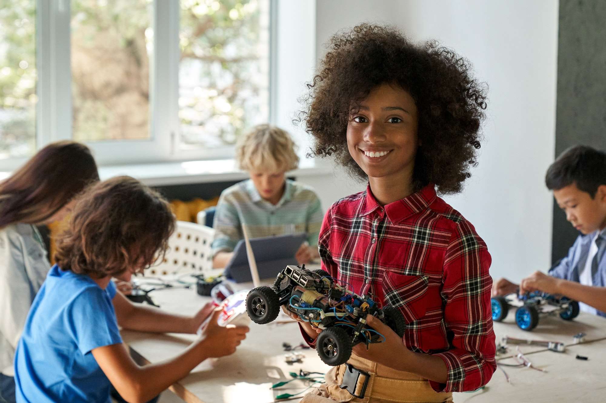 Happy African American kid school girl holding robotic car at STEM class.